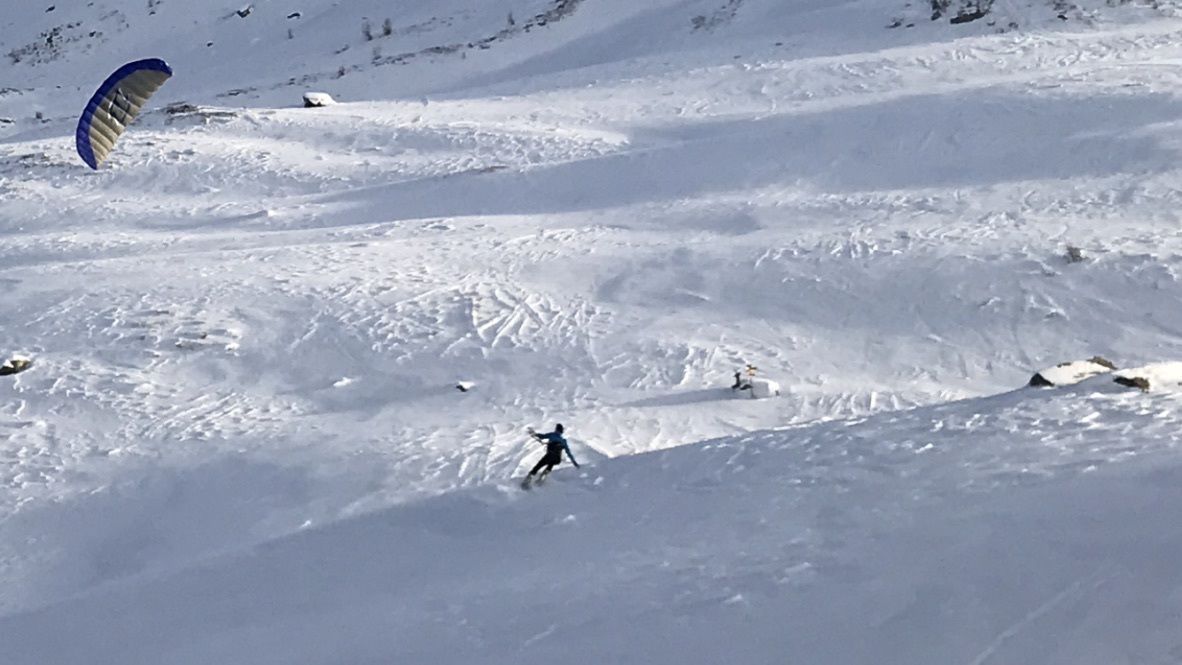 Eine verschneite Landschaft mit einer Person beim Skifahren und einer Drachen im Flug.