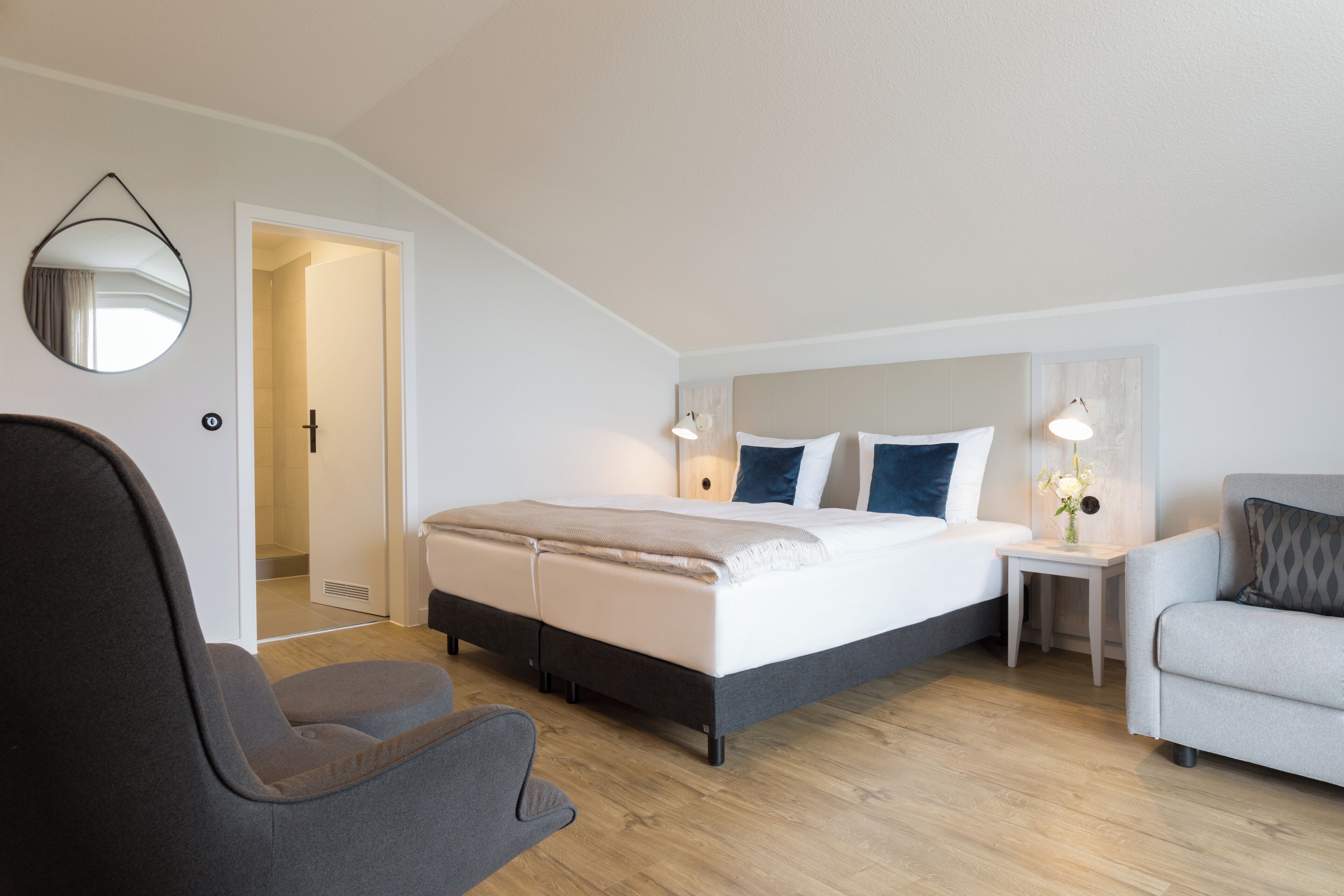 Une chambre à coucher moderne avec un lit, deux tables de chevet, une chaise et un miroir au mur.