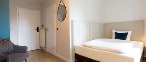 A bedroom with a bed, a chair, a door, and a mirror.