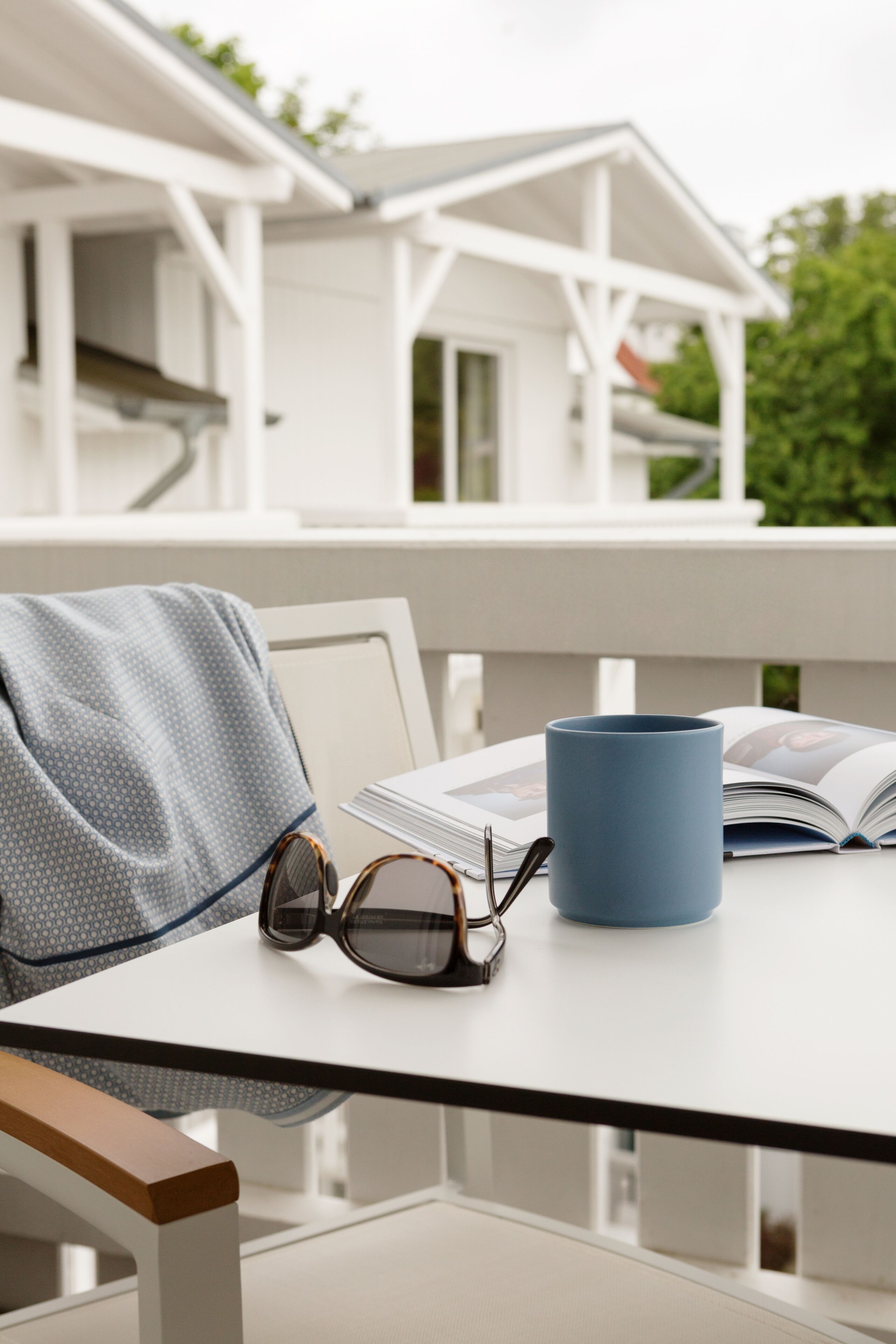 Una mesa con una taza azul, unos lentes de sol y una revista abierta.