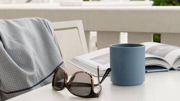 Una mesa con una taza azul, unos lentes de sol y una revista abierta.