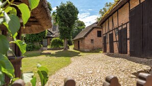 A cobblestone pathway leading to a traditional building with a thatched roof and brick walls. - Koopmanns Hotel und Lädchen (Göhren)