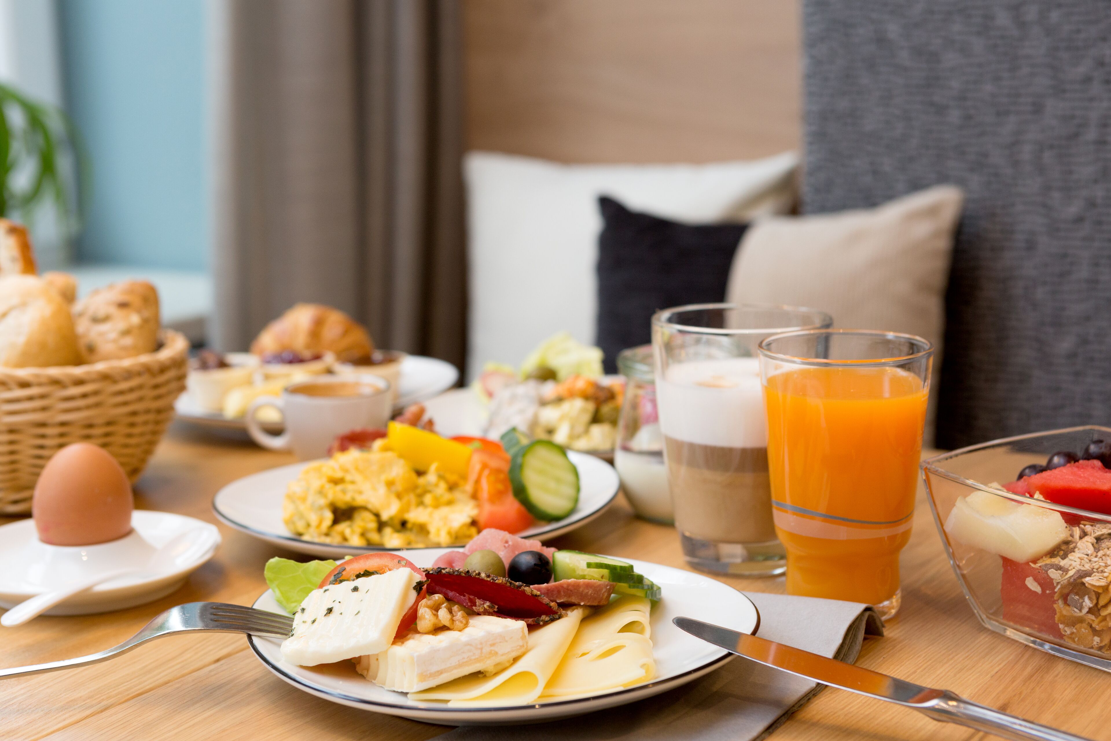 A breakfast setting with various dishes, including eggs, toast, and fruit, on a wooden table.