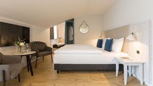 A modern hotel room with a large bed, a seating area with a table, and a mirror on the wall. - Koopmanns Hotel und Lädchen (Göhren)
