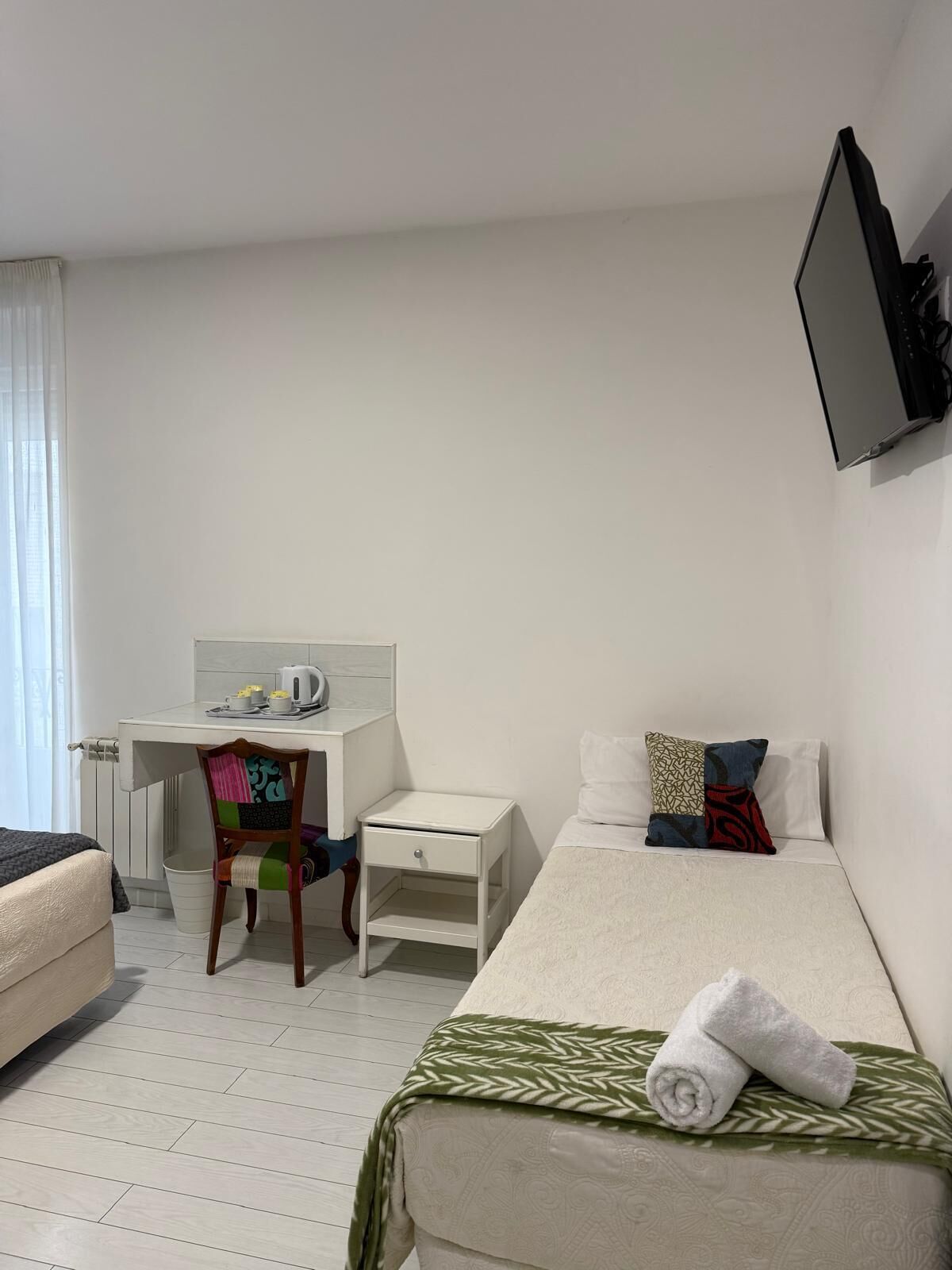 Une chambre d’hôtel équipée d’un lit, d’un bureau, d’une chaise, d’une petite table de chevet et d’un téléviseur fixé au mur.