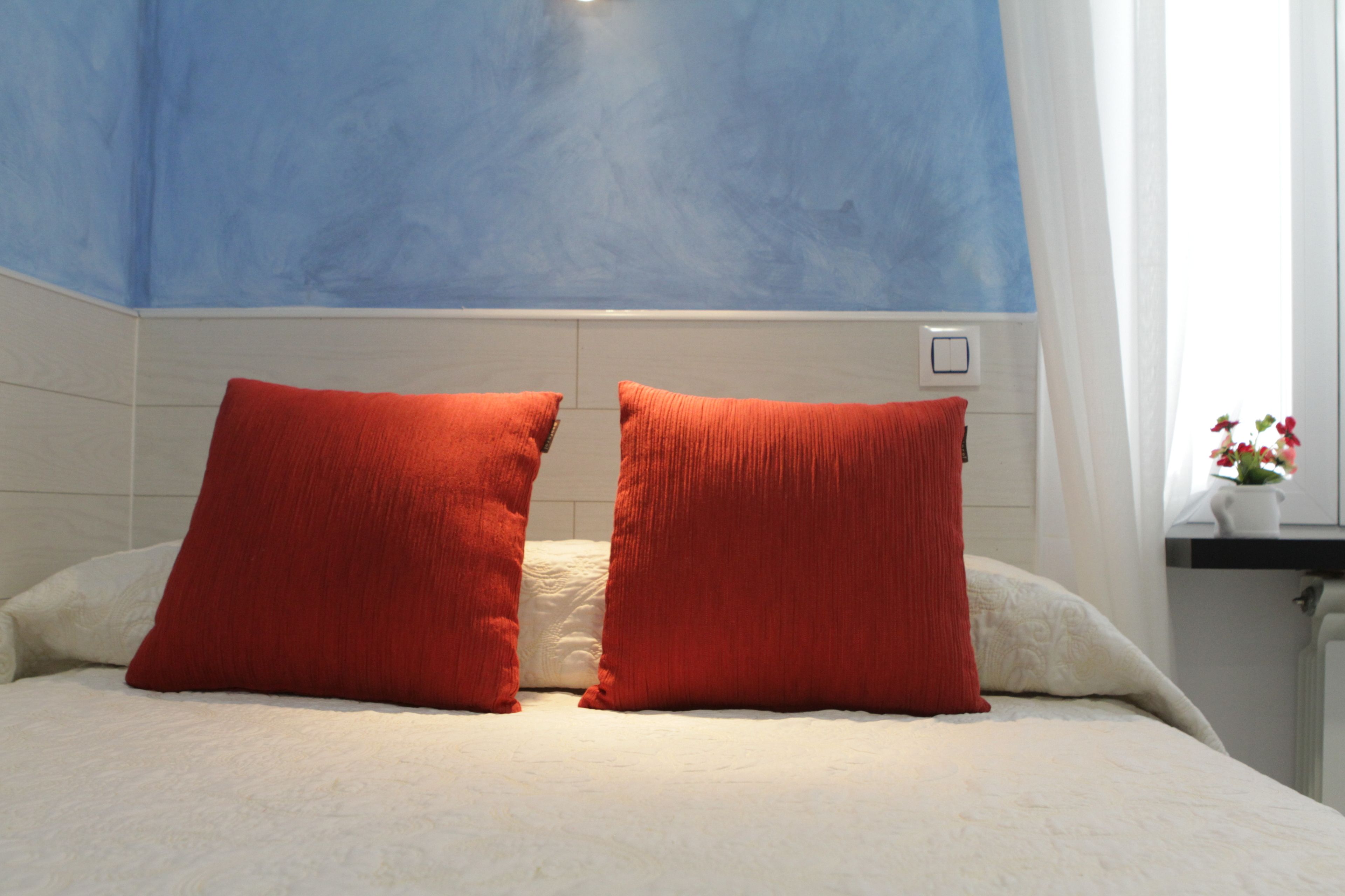 A bed with two red pillows, a white headboard, and a blue ceiling.