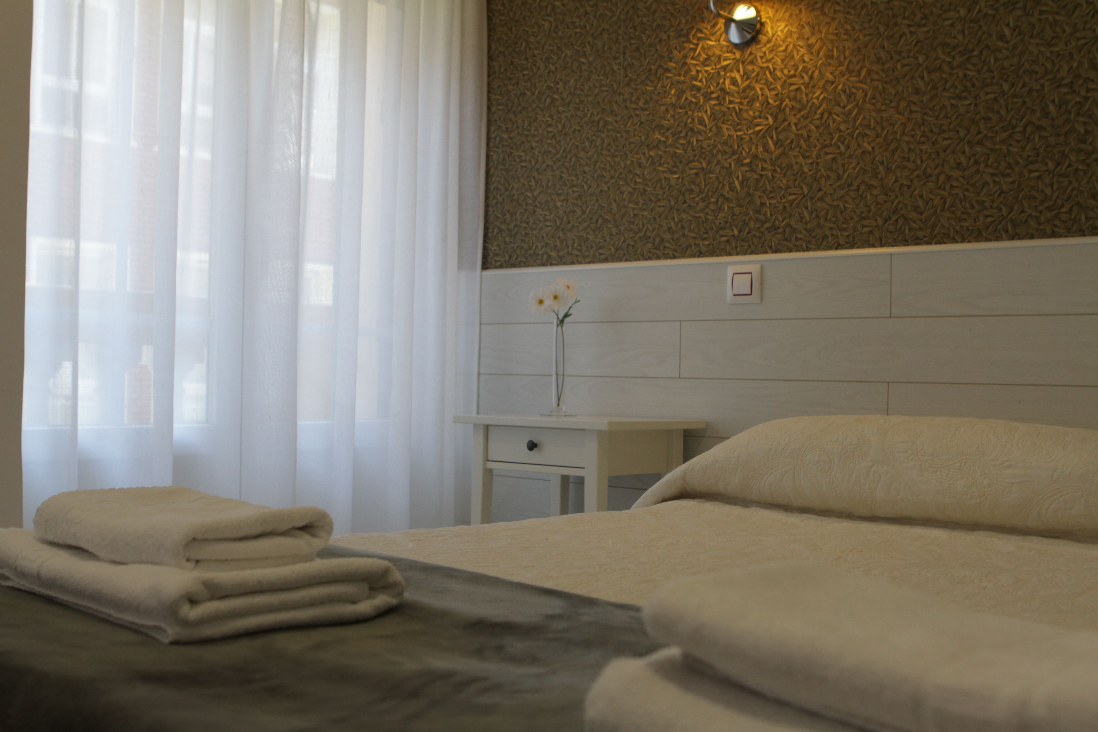 A hotel room with a bed, a nightstand, a vase with a flower, and a wall with a textured pattern.