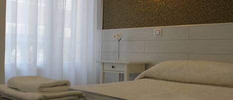 A hotel room with a bed, a nightstand, a vase with a flower, and a wall with a textured pattern.