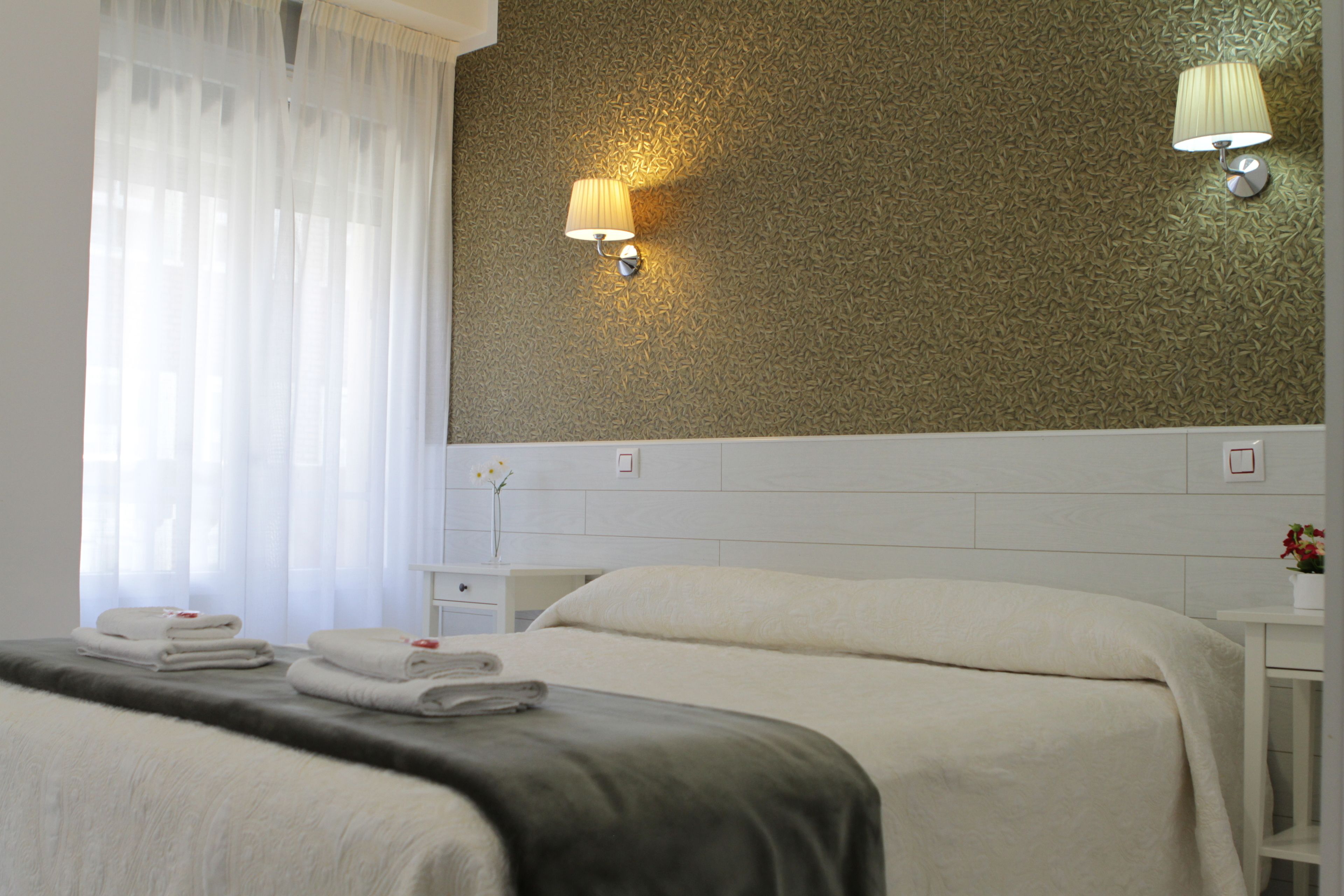 A hotel room with a neatly made bed, a nightstand with a lamp, and a wall with a textured pattern.