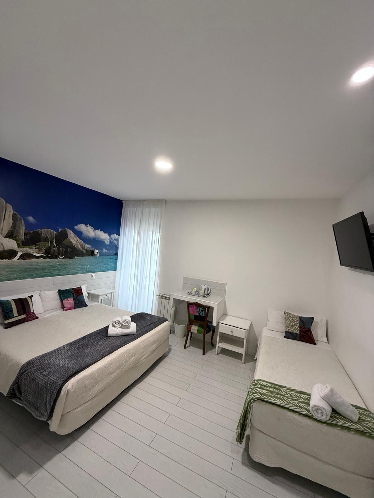 A hotel room with a large bed, a smaller bed, a desk, and a TV.