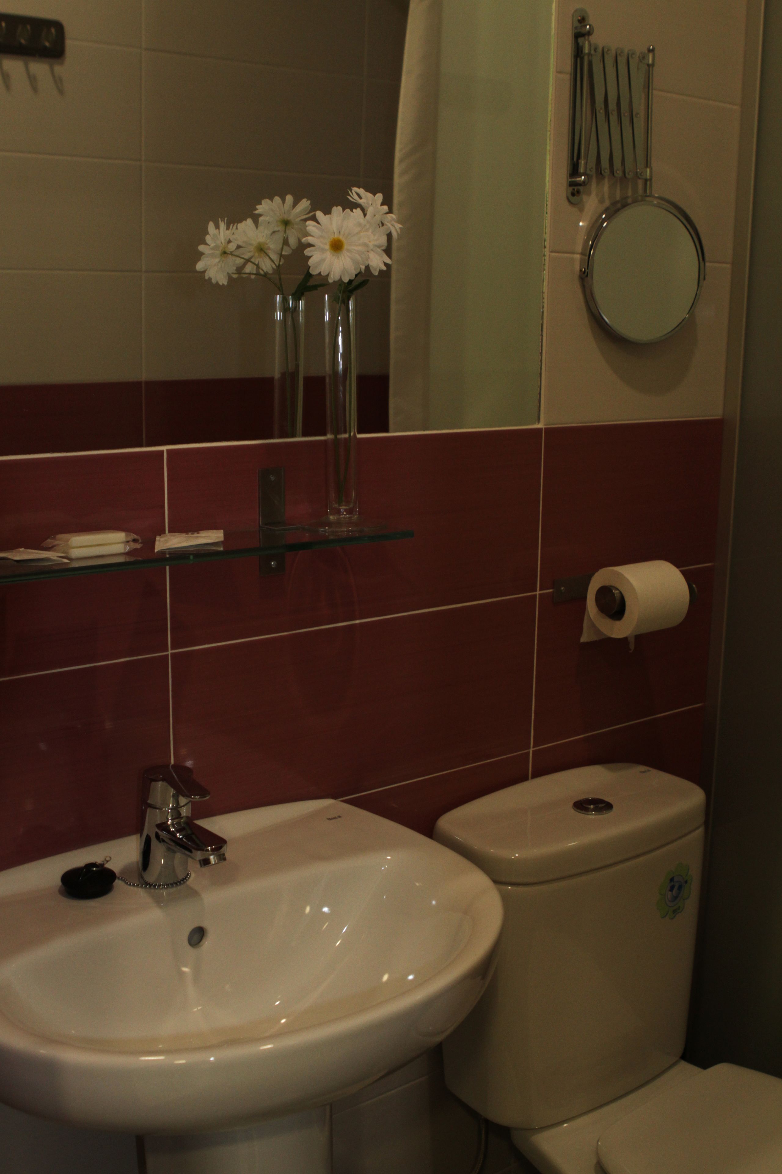 A bathroom with a sink, toilet, and a mirror. There are white flowers in a glass vase on the sink.