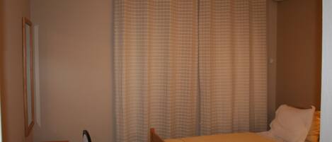 Un dormitorio con una cama, una silla, un espejo y una ventana con cortinas.