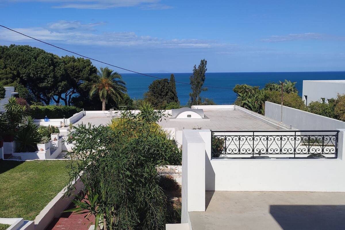 A residential area with a view of the sea, white buildings, and a well-maintained lawn.