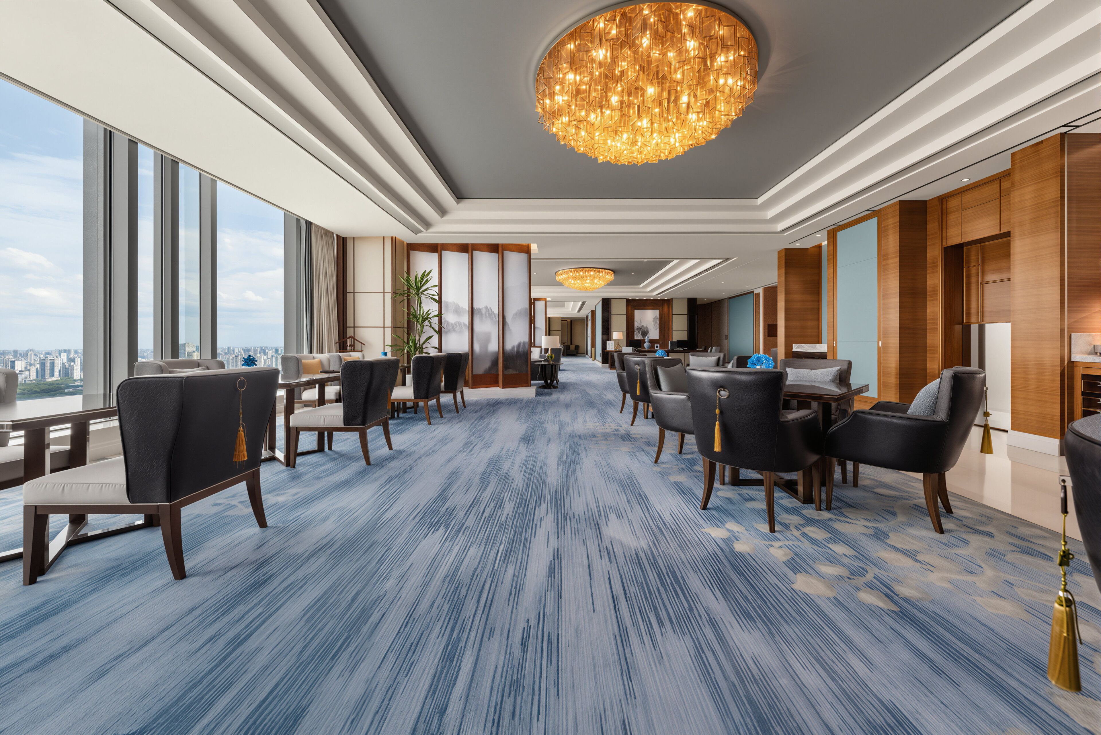 Un moderno vestíbulo de hotel con una alfombra de estampado azul, amplias ventanas que ofrecen vistas a la ciudad y una araña.