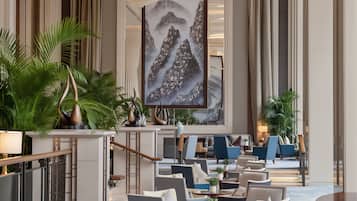 Um hall de hotel com áreas de estar, uma pintura grande e plantas decorativas.