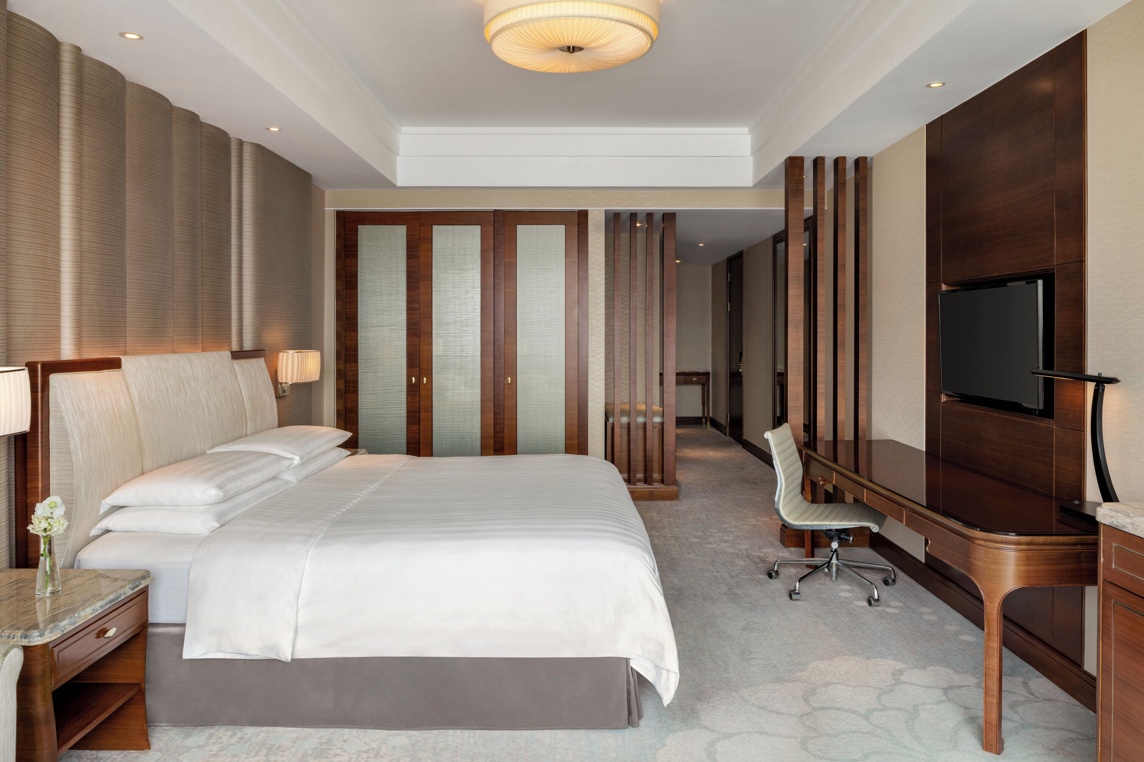 Una habitación de hotel moderna con una cama grande, un escritorio, una silla, un televisor y un armario.