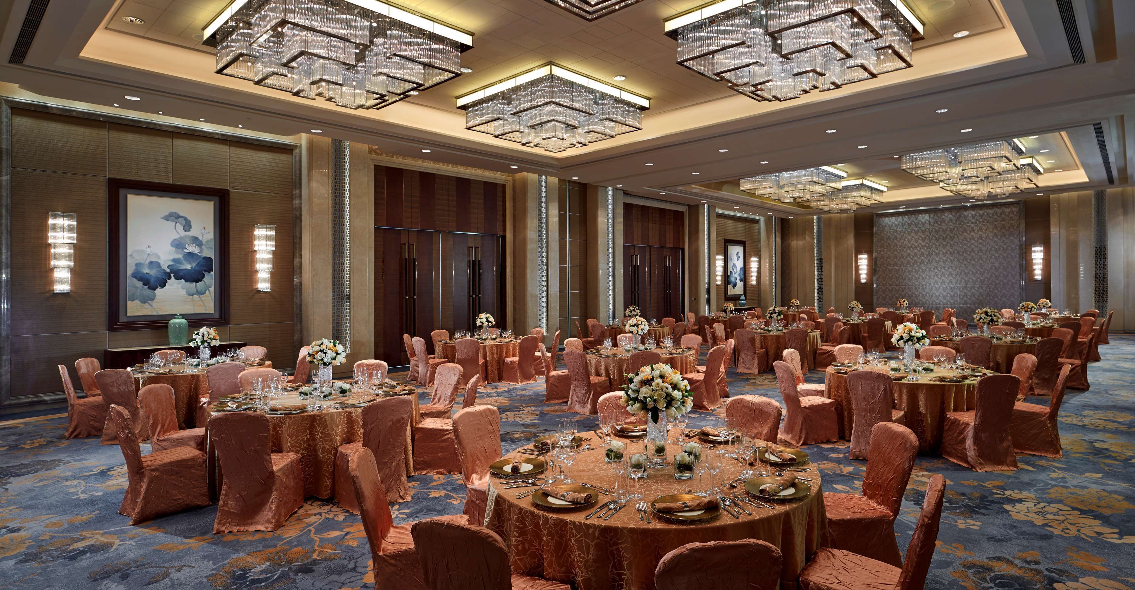 A large banquet hall with round tables, chairs, and chandeliers.