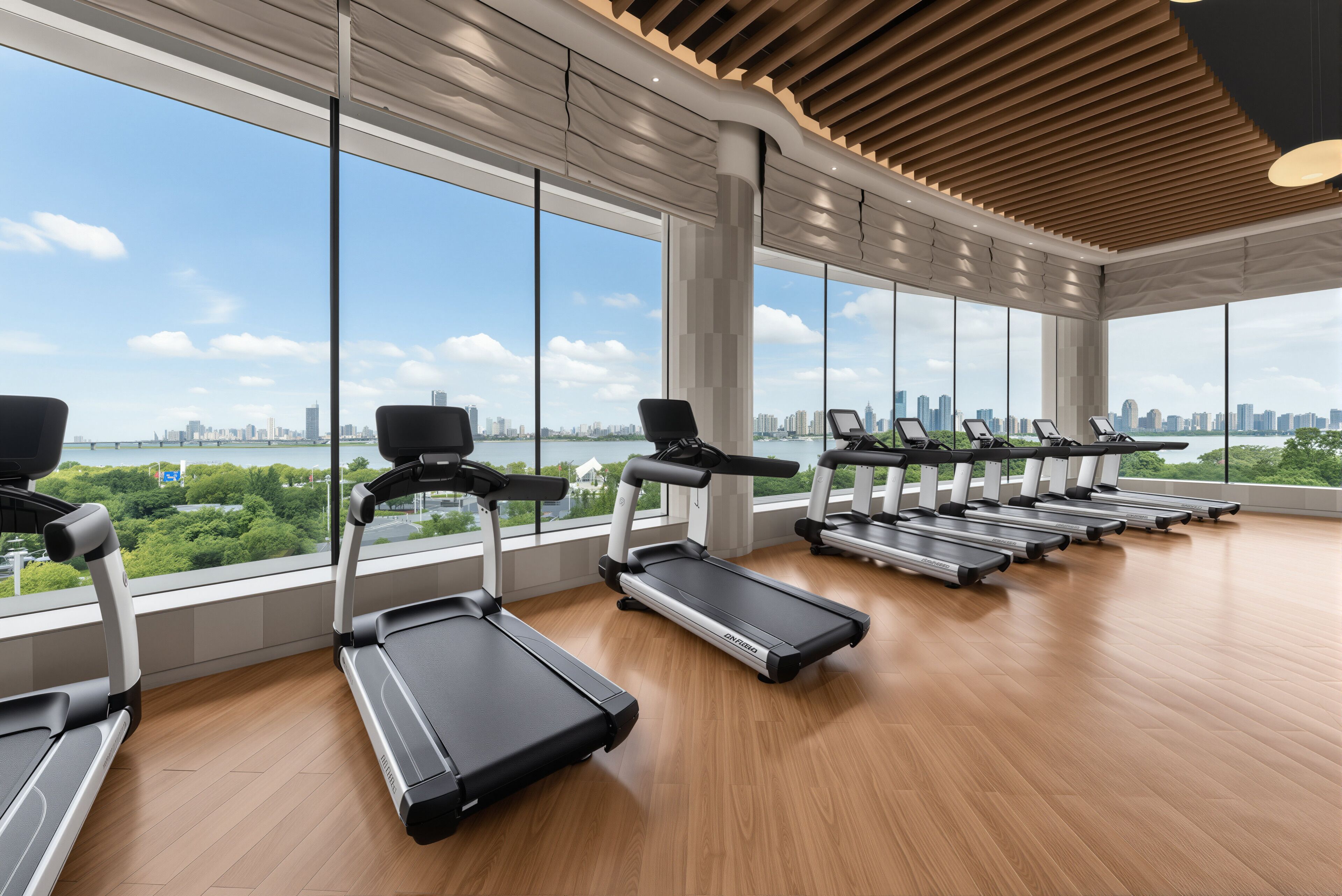 A gym with treadmills aligned against a wall with large windows offering a cityscape view.