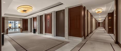 A hotel corridor with a central elevator, wooden paneling, and a carpeted floor.