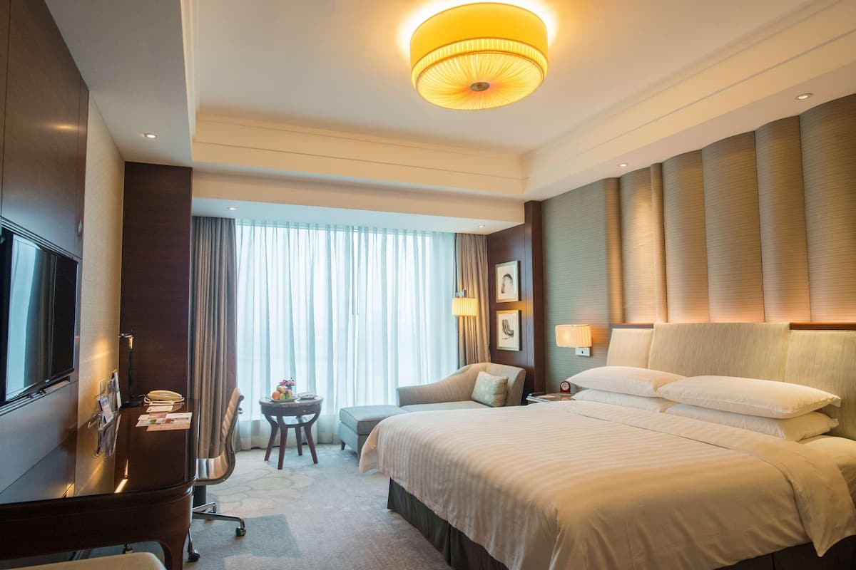 A hotel room with a bed, a desk, a television, and a window with curtains.