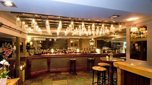 A bar area with hanging light fixtures, stools, and a bar counter. - The Chapter House (Salisbury)