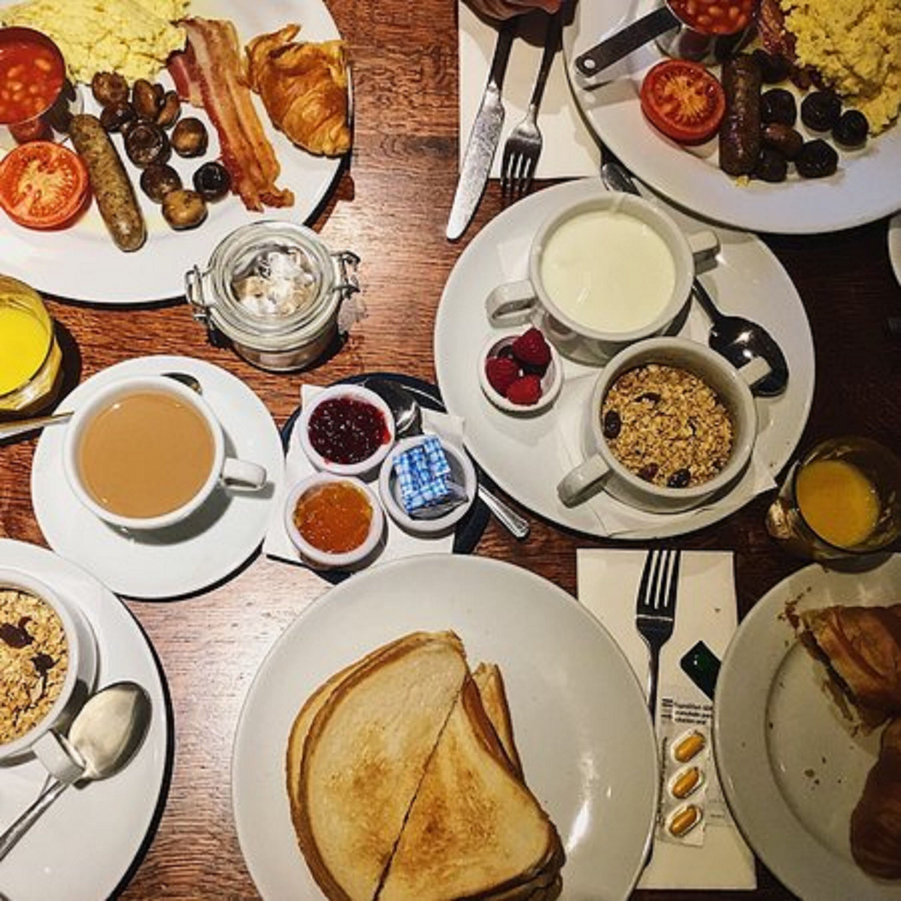 A breakfast table with various dishes including toast, eggs, sausages, and a variety of spreads.