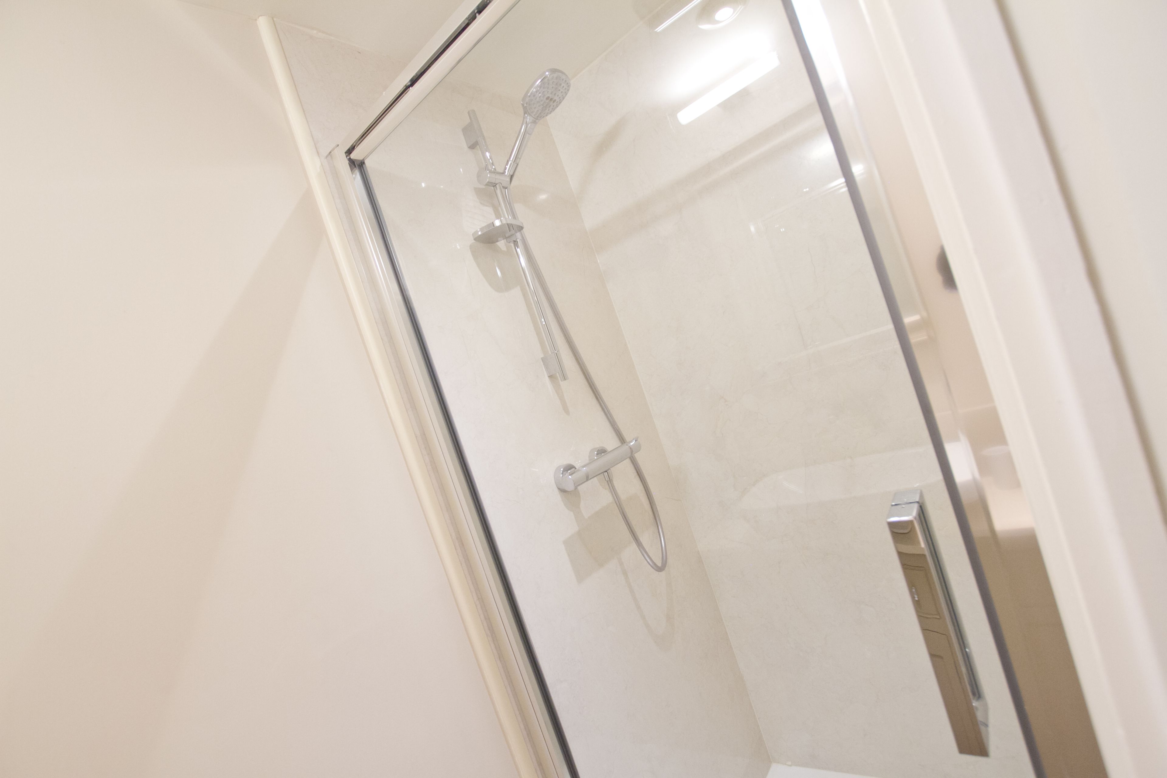A glass-enclosed shower with a handheld showerhead and a wall-mounted faucet.