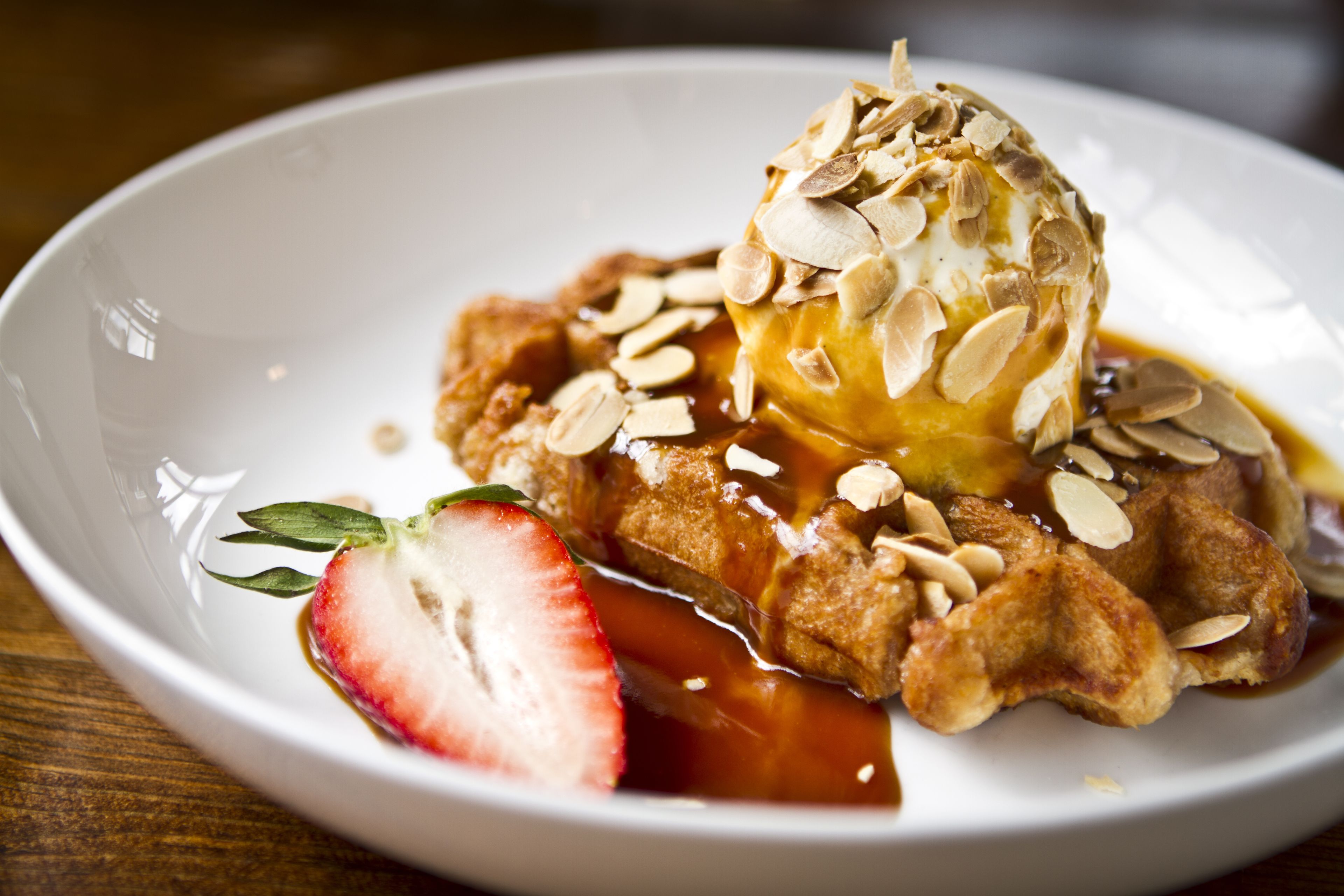 A plate of French toast with sliced almonds and a strawberry on the side.