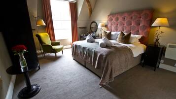 A bedroom with a large bed, a chair, a table, and a vase with flowers.