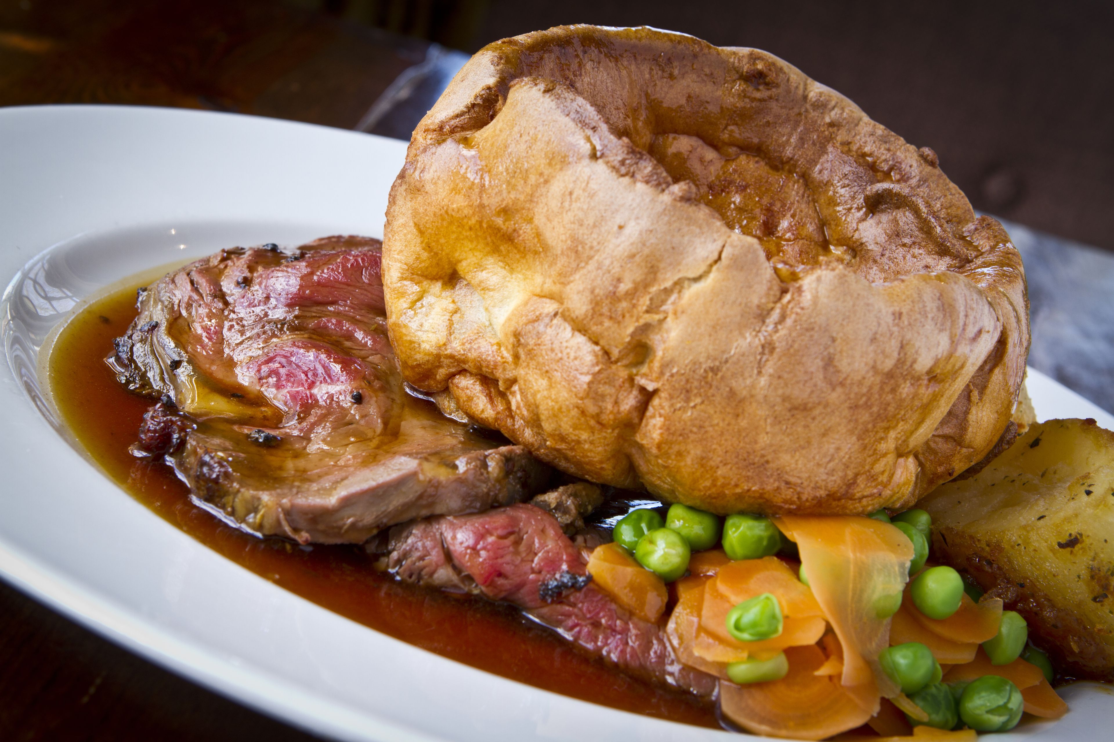 A plate with roast beef, Yorkshire pudding, peas, carrots, and potatoes.