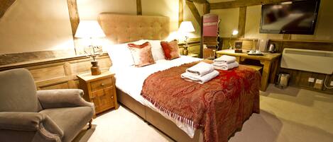 A bedroom with a large bed, a wooden chair, a desk, a television, and a radiator.