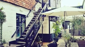 An outdoor patio area with a staircase leading to an upper level, surrounded by tables and chairs, and potted plants. - The Chapter House (Salisbury)