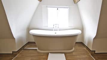 A modern bathroom with a freestanding bathtub, a window, and wooden flooring.