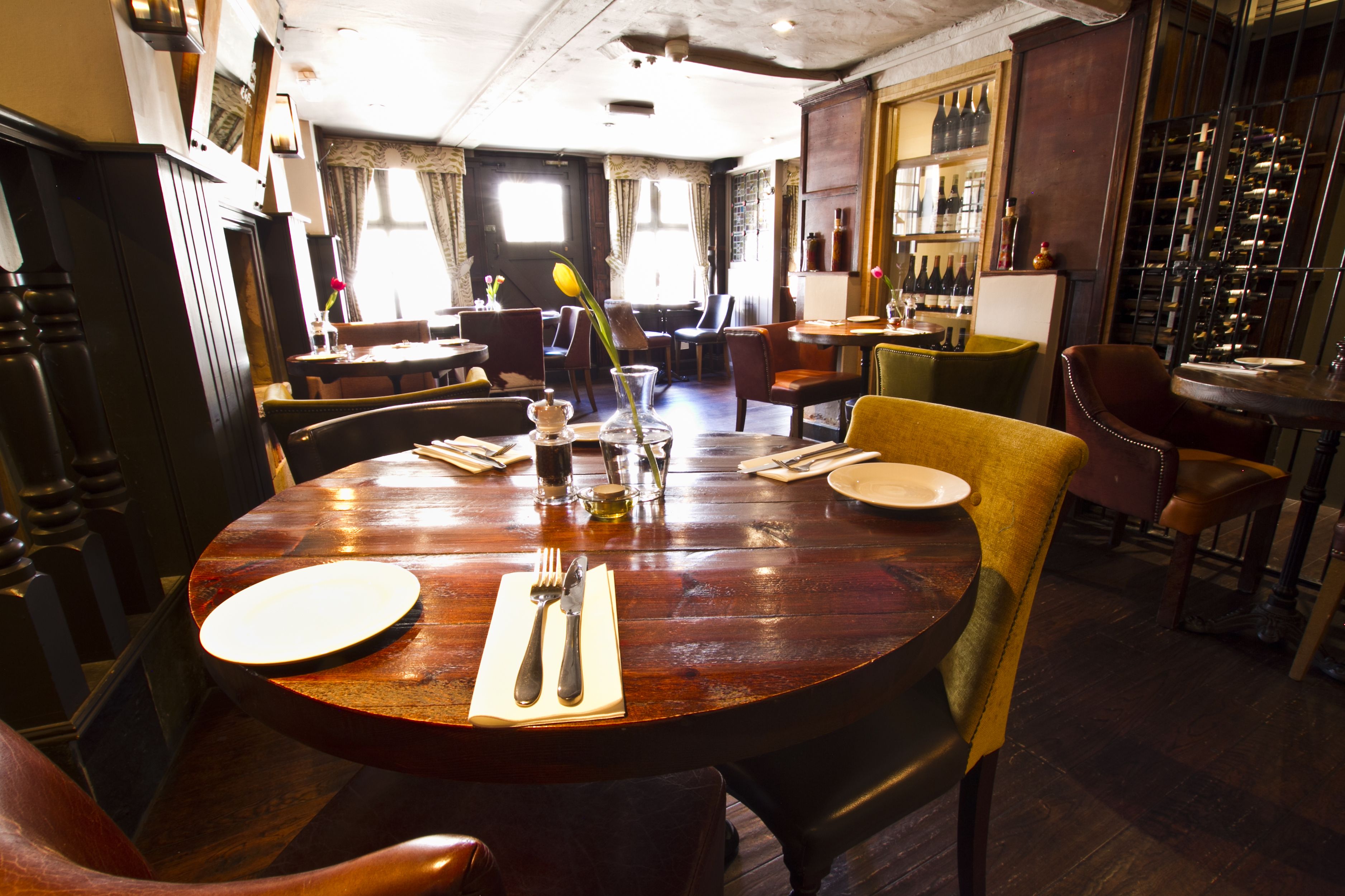 A restaurant with a wooden dining table set for two, surrounded by chairs.