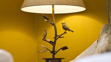 Una lámpara con pantalla texturizada y una rama con pájaros, sobre un muro amarillo.