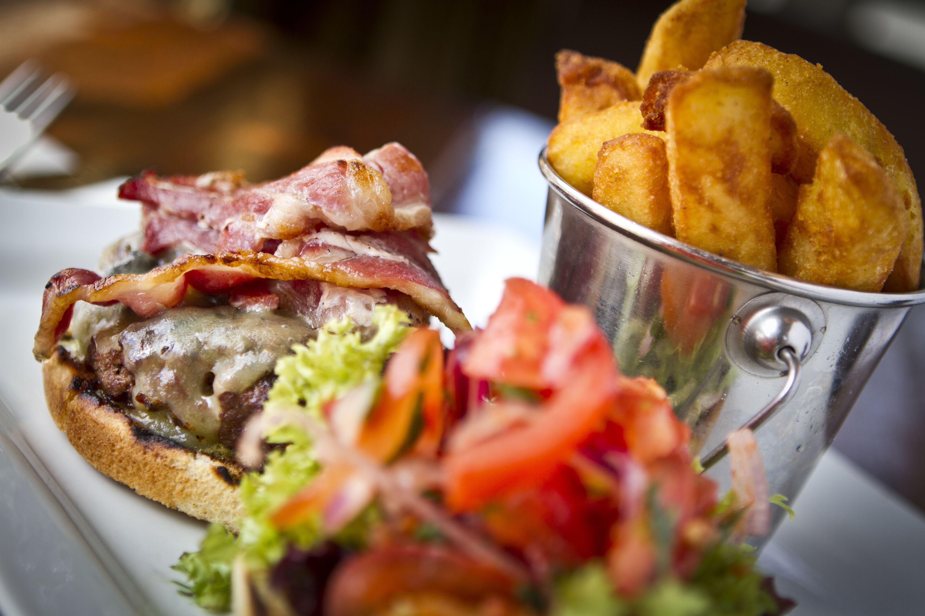 A plate with a sandwich, a side salad, and a small metal container of potato wedges.