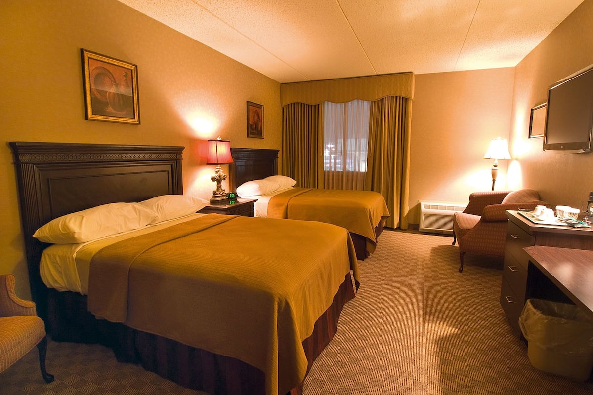 Ein Hotelzimmer mit zwei Betten, einem Schreibtisch, einem Sessel, einem Fernseher und einem Fenster mit Vorhängen.