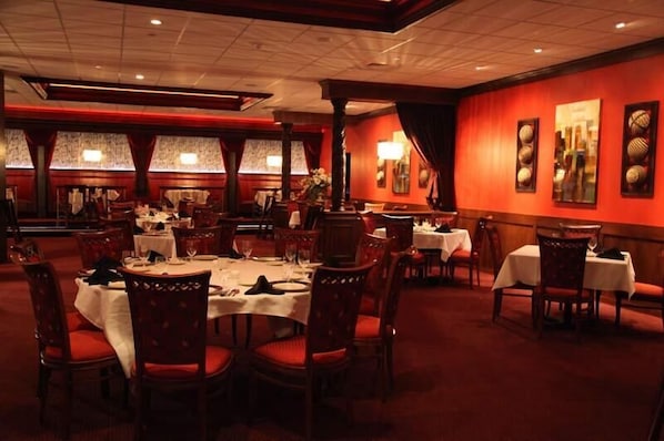 Un restaurant avec des tables rondes, des chaises rouges et un mur rouge orné d’œuvres d’art encadrées.