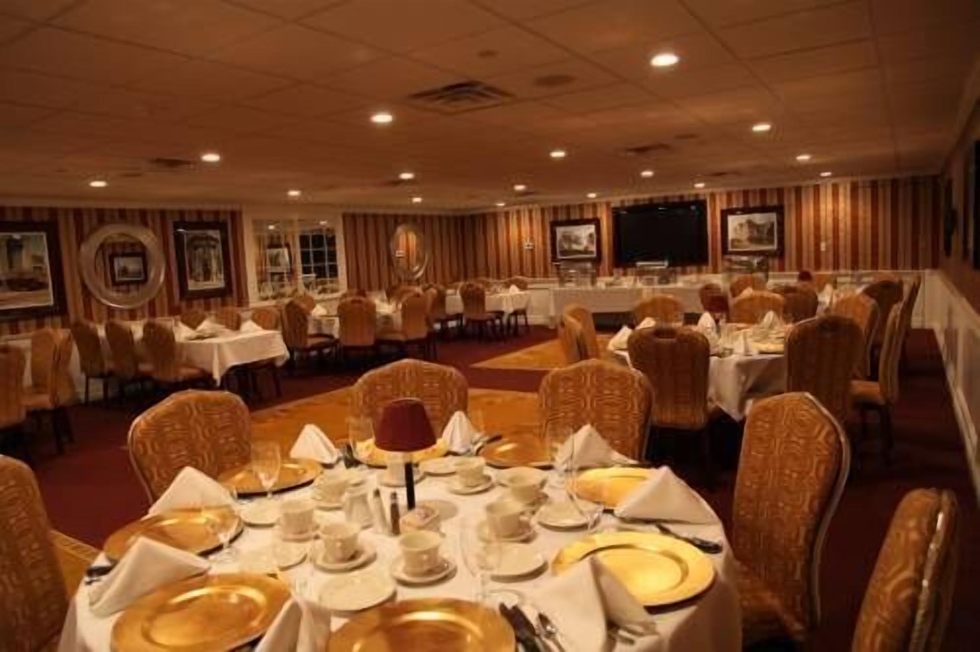 A banquet hall with round tables set for dining, featuring white tablecloths, gold-rimmed plates, and wicker chairs.