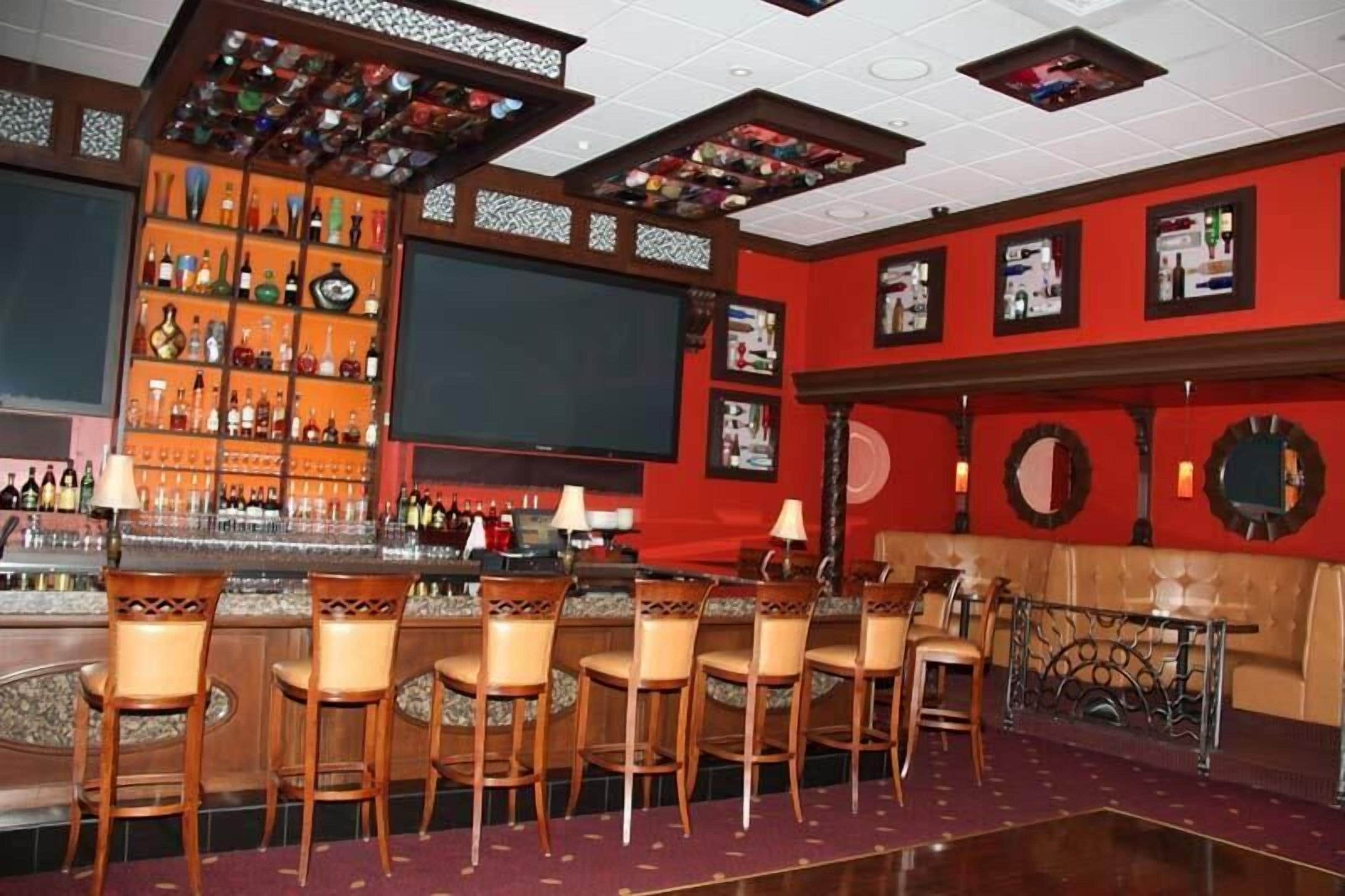 Una zona de bar con varios taburetes, una barra y una estantería con diferentes botellas.