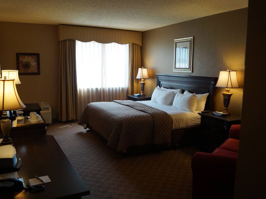 A hotel room with a large bed, two bedside tables with lamps, a desk with a telephone, and a chair.