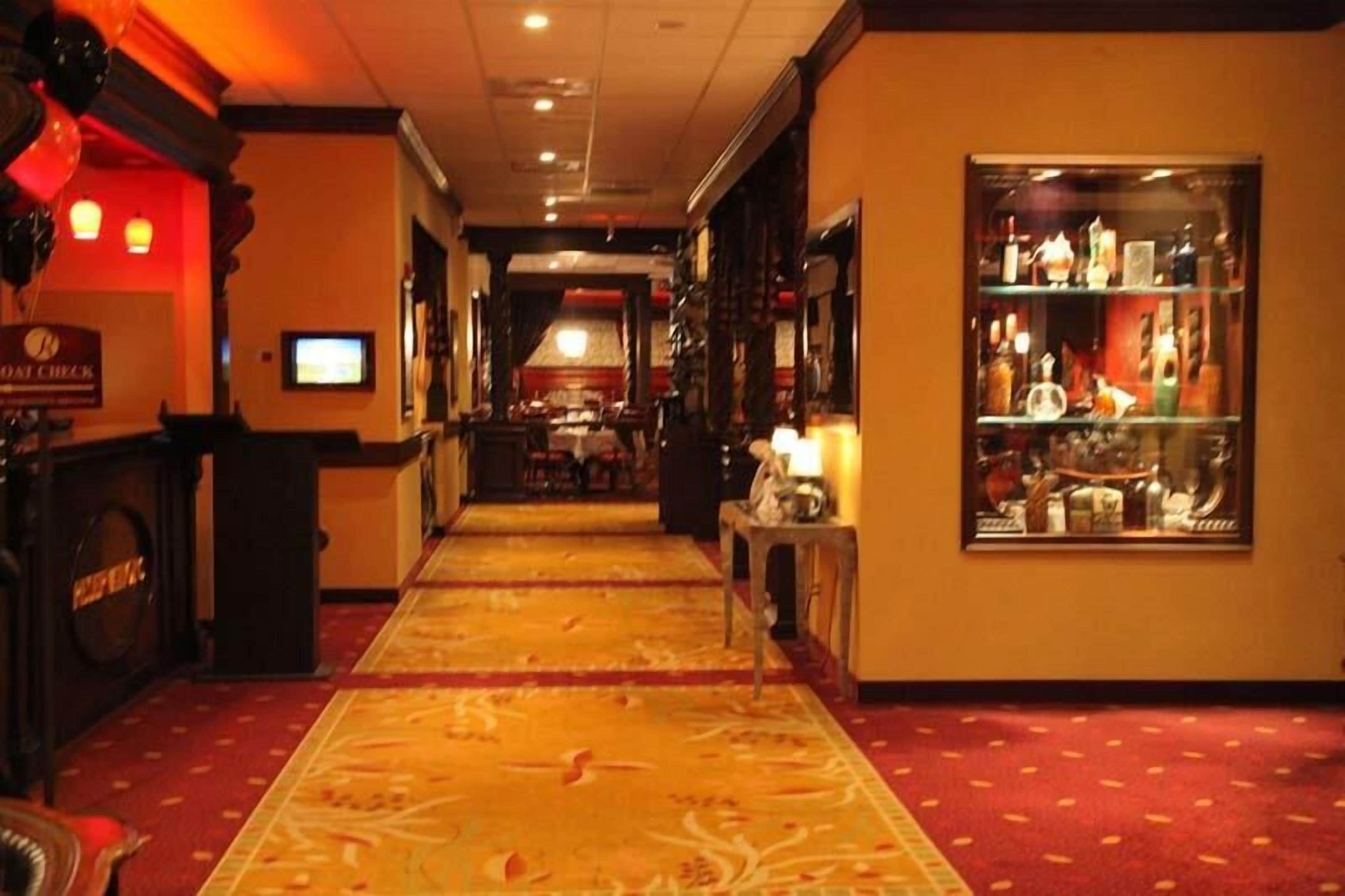 Un couloir d'hôtel avec un sol recouvert de moquette, un comptoir de réception, un coin bar et une vitrine contenant des bouteilles.