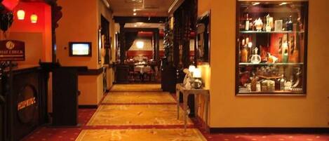 Un pasillo de hotel con suelo alfombrado, mostrador de recepción, zona de bar y una vitrina con botellas.