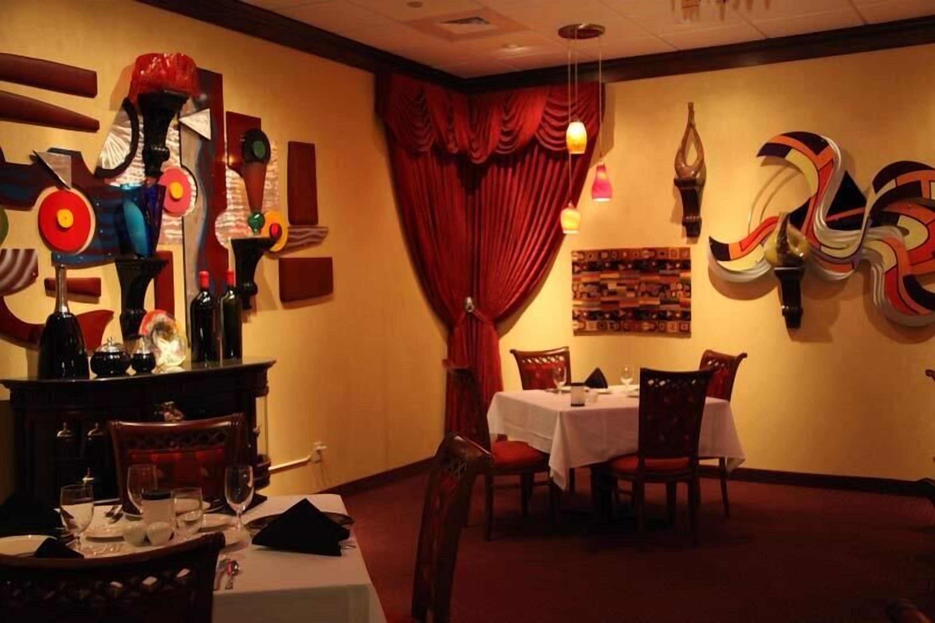 A dining area with tables set for two, red curtains, and abstract wall art.
