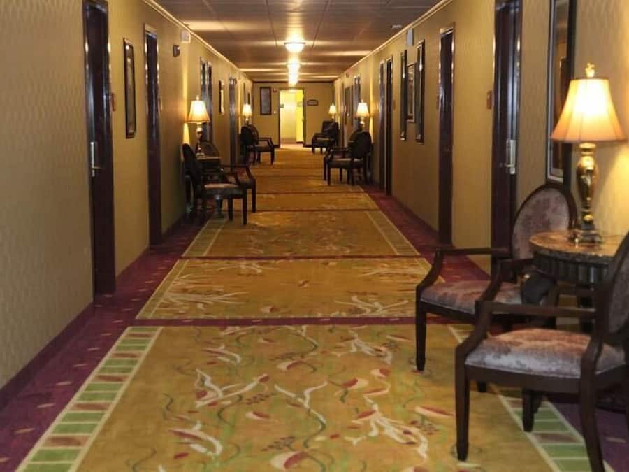 A hotel hallway with carpeted floors, chairs, and lamps.