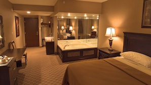 Een hotelkamer met een groot bed, een bureau met stoel, een badkamer met bad en een spiegel.