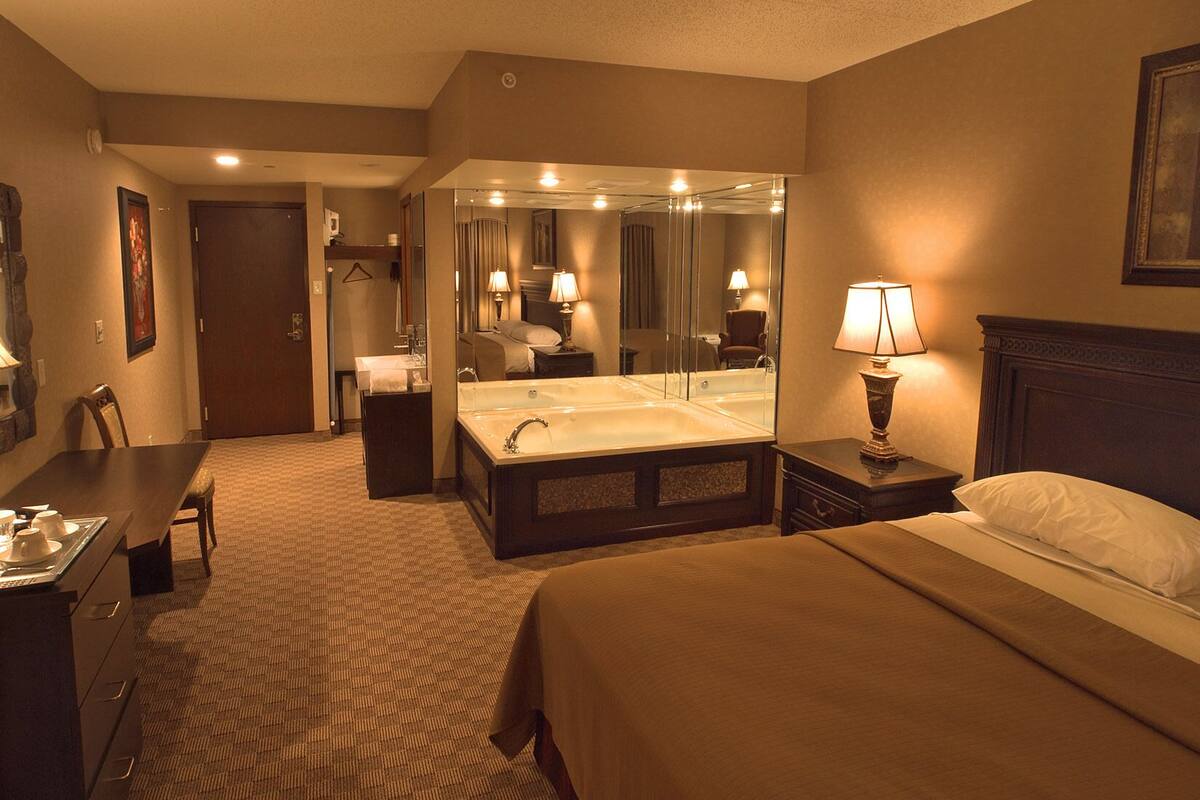 Ein Hotelzimmer mit einem großen Bett, einem Schreibtisch mit Stuhl, einem Badezimmer mit Badewanne und einem Spiegel.