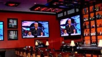 A bar with multiple televisions displaying a show, a bar counter, and shelves with bottles.