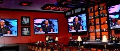 A bar with multiple televisions displaying a show, a bar counter, and shelves with bottles.