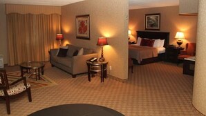 Een hotelkamer met een bank, een bed, een bureau en een stoel. Er staan lampen op het bureau en de nachtkastjes.
